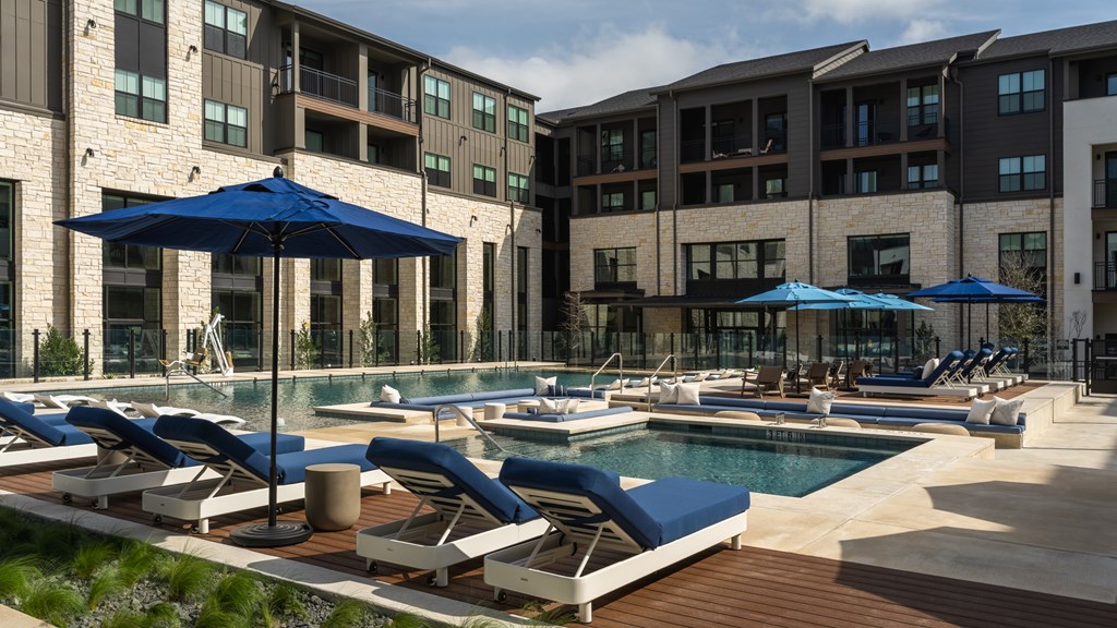 A pool area with sun loungers and umbrellas in front of a building.